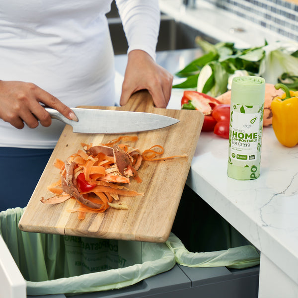 Home Compostable 35L Kitchen Bin Liner. Perfect for lining your home or business pull out kitchen bin. Picture showing food scraps being scraped into the bin from a chopping board.
